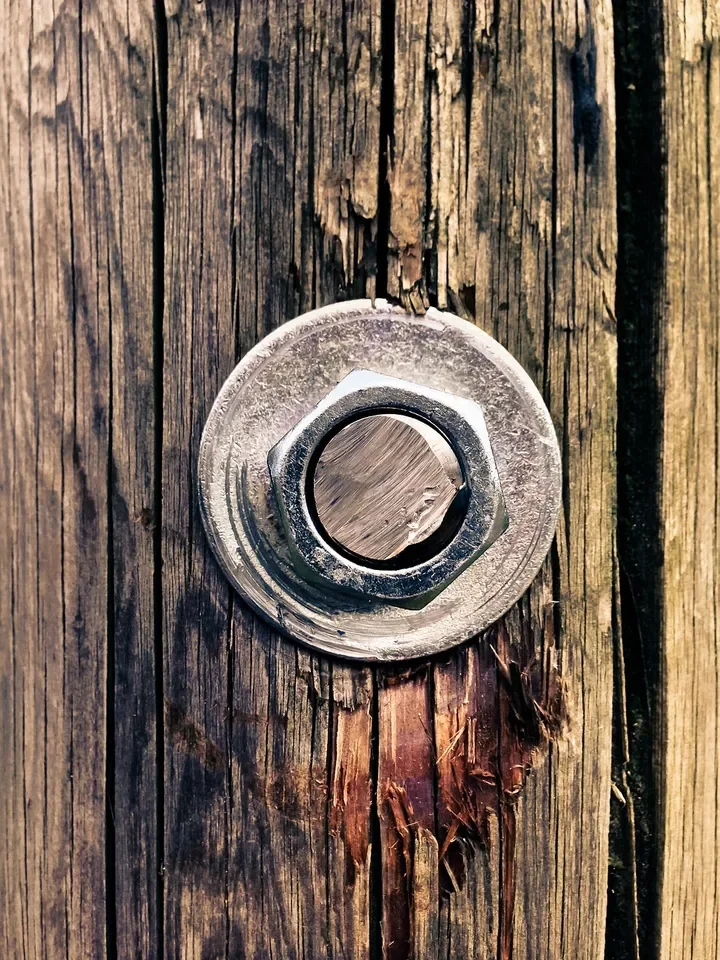 Flat washer under a hex nut on a bolt through a weathered wood board