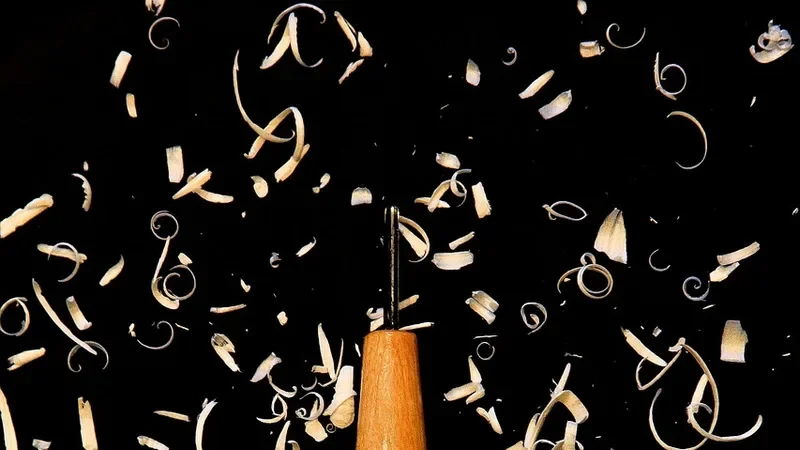 Fine hand carving tool surrounded by fresh wood shavings on a black background
