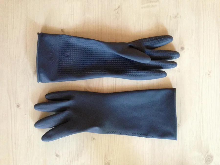 Rubber gloves for wood bleaching pair of heavy rubber chemical gloves laid on a light pine board