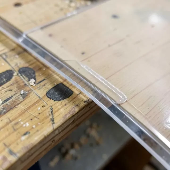 Clear adhesive being applied along the edge of an acrylic sheet before bonding it to wood