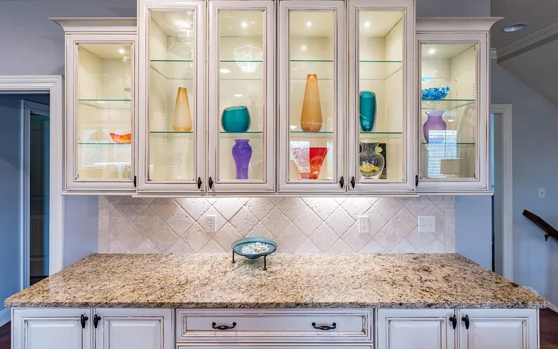 White painted plywood kitchen cabinets with glass display doors and granite counter