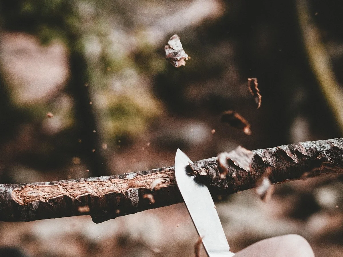 Knife slicing bark from a green stick with shavings flying