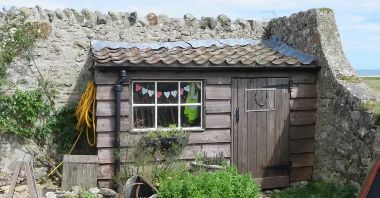 Small wooden lean-to style shed with a single sloped roof built against a stone wall
