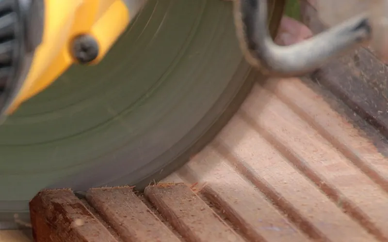 Miter saw blade cutting through a grooved deck board