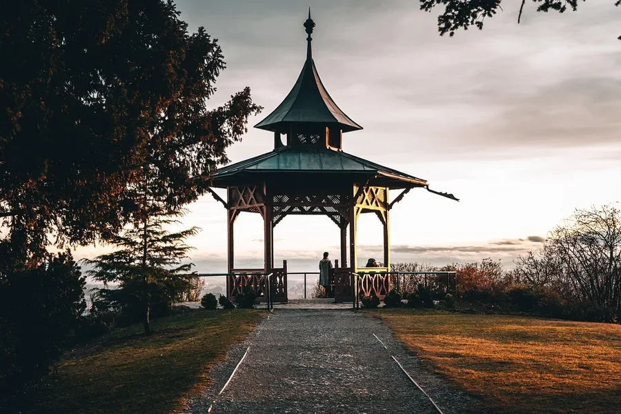 Wooden garden pavilion with a multi-sided roof at sunset