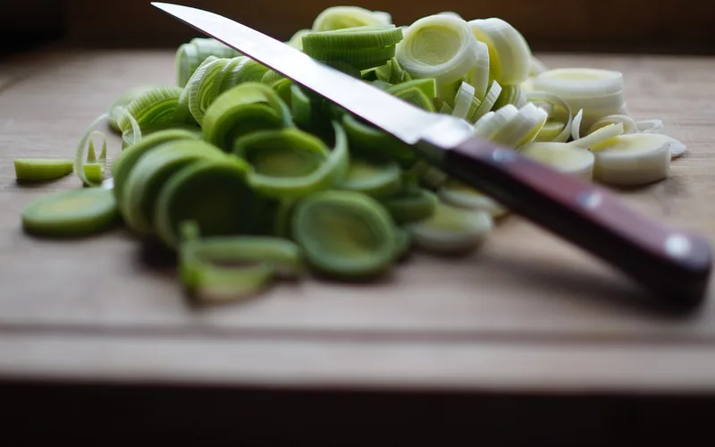 wooden cutting board with sliced leeks and a kitchen knife during food prep wooden cutting board with sliced leeks and a kitchen knife during food prep