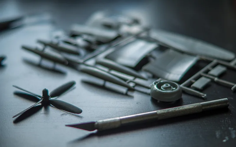 Clear plastic model kit parts and glue being assembled by hand on a hobby workbench