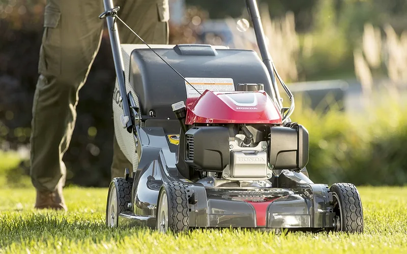 gas push mower with red engine being used on a freshly mowed lawn