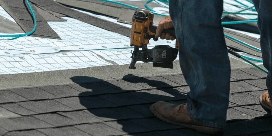 Roofer using a pneumatic nail gun to install asphalt shingles