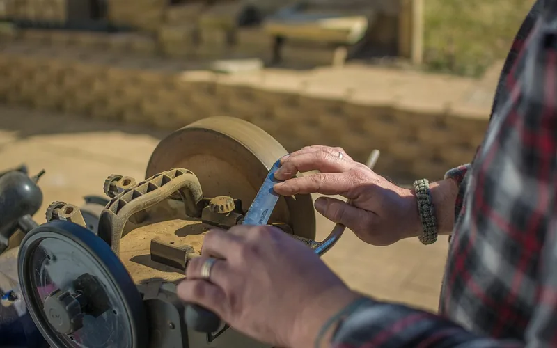 hand holding a metal blade against a bench grinder wheel to sharpen the edge
