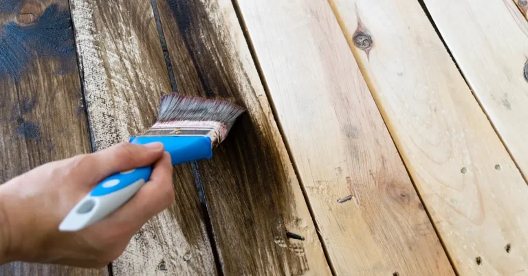 Hand brushing dark wood stain next to an unstained lighter section on a plank