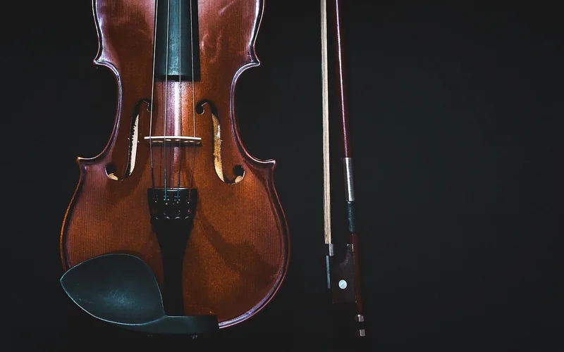 Violin with a glossy hand-finished wood body and a bow against a dark background
