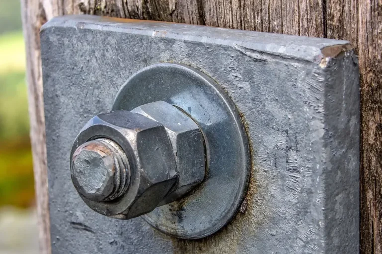 Steel bolt with a flat washer and hex nut fastened through a wooden post