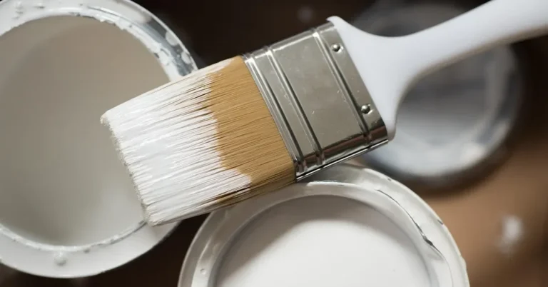 Paintbrush loaded with white primer resting on open paint cans