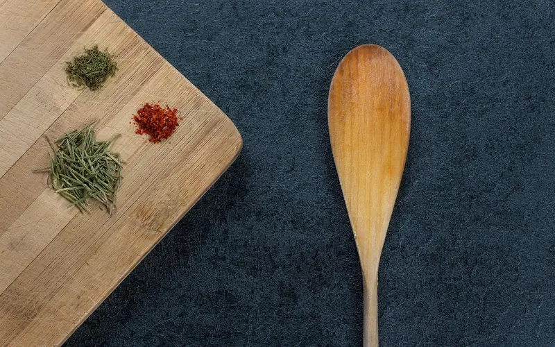 Wooden spoon beside a maple cutting board with dried herbs on a dark counter Wooden spoon beside a maple cutting board with dried herbs on a dark counter