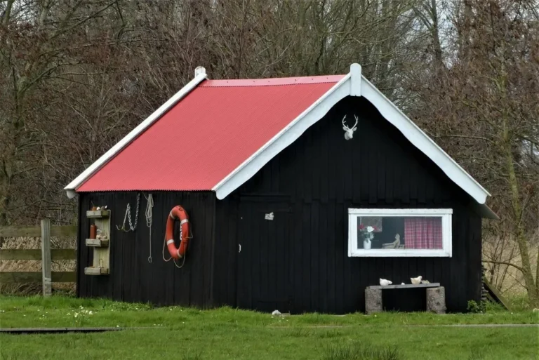 Small wooden shed with a red metal gable roof standing on a lawn