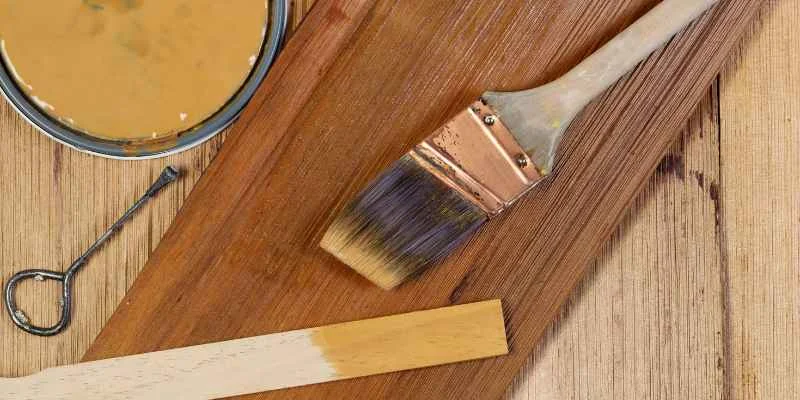 can of oil-based wood stain with a natural-bristle brush and a bare wood board being finished