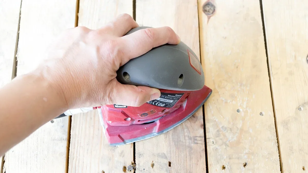 Sanding a wood plank surface with an orbital sander after a filler repair has cured