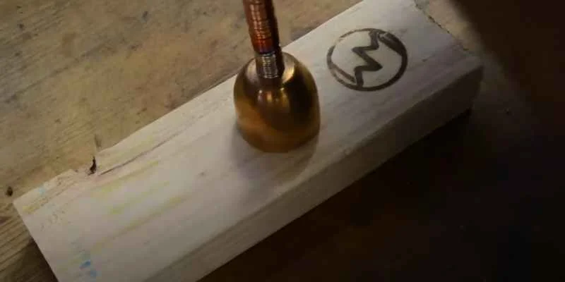 Electric branding stamp pressing a circular logo design into pine wood
