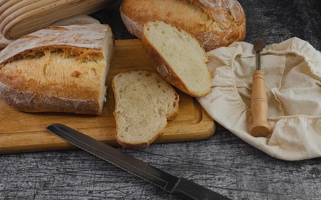 Bread being sliced with a knife directly on a wooden cutting board