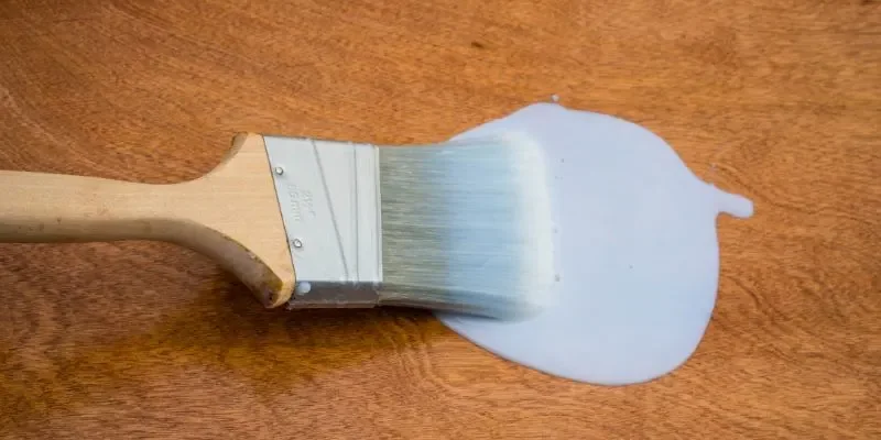 Brush applying milky white water-based polyurethane to wood