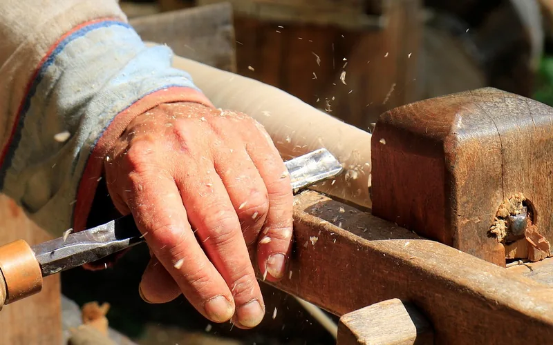 Hand chiseling a wood edge, wood shavings flying off the blade