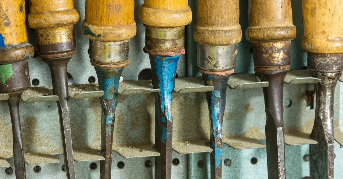 Wood-handled chisels hanging in a row on a workshop pegboard