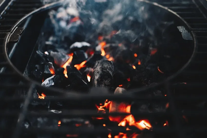 glowing charcoal and wood embers with smoke rising in a grill