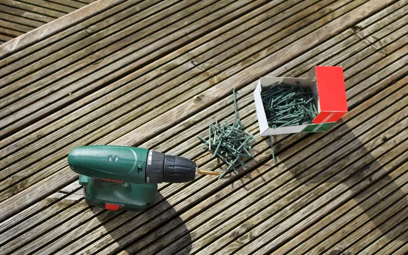 cordless drill and a box of deck screws on a wood plank cordless drill and a box of deck screws on a wood plank