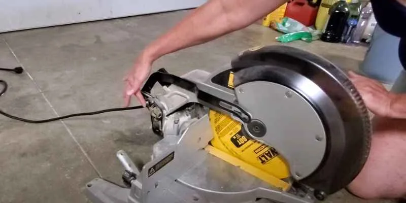 Hand reaching for the transport lock pin near the hinge of a DeWalt chop saw