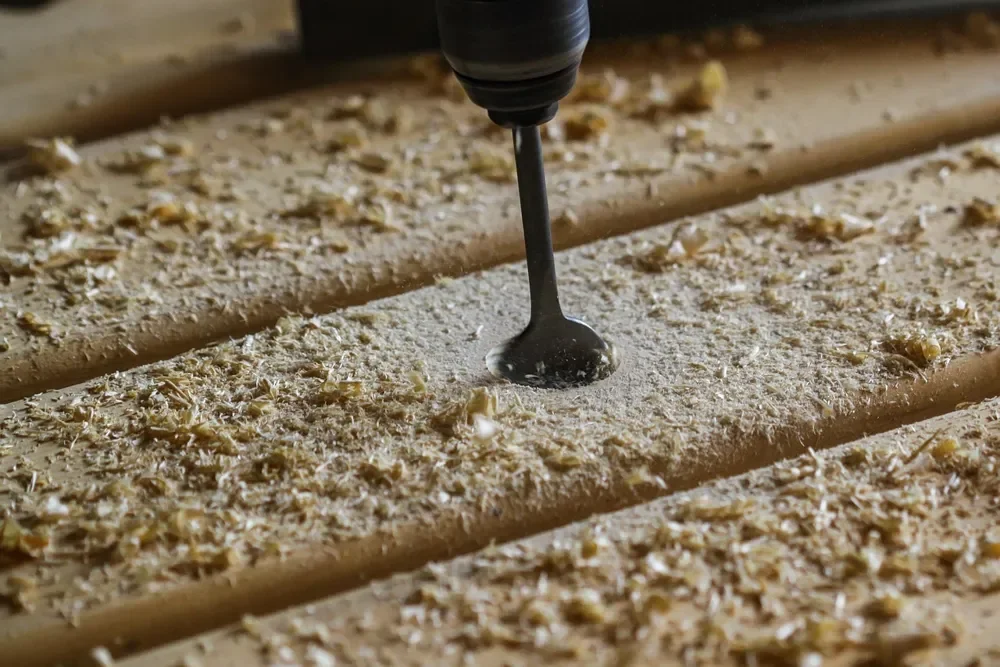 Drill bit boring into a wood board surrounded by wood chips