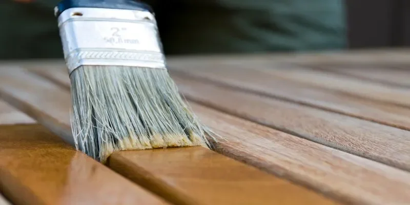 brushing wood stain onto outdoor deck boards with a paintbrush