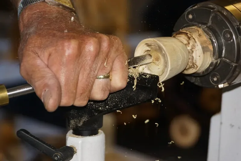 Turner cutting a bowl blank mounted on a lathe chuck with the tool rest set close Turner cutting a bowl blank mounted on a lathe chuck with the tool rest set close