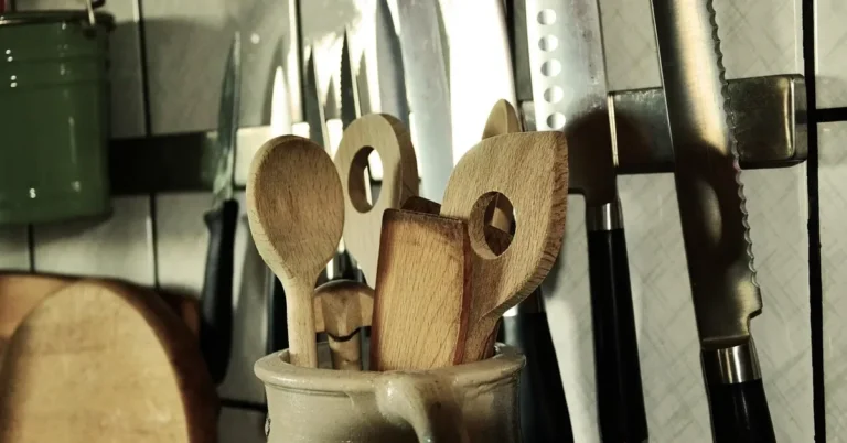 Wooden spoons and spatulas in a stoneware crock beside kitchen knives