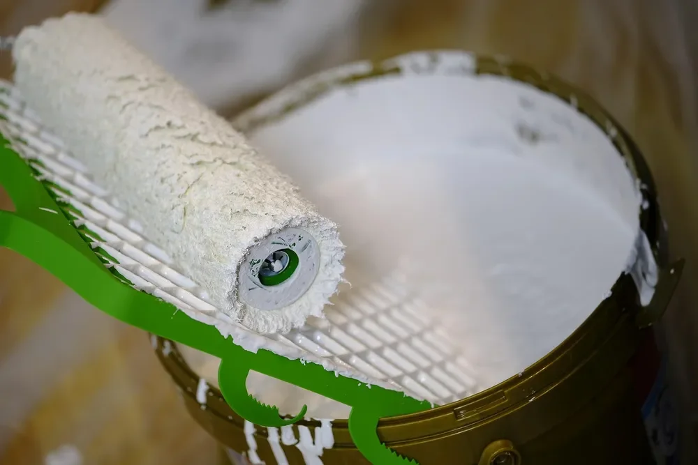 Paint roller resting on a tray of white paint