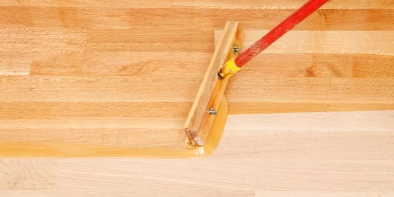 Applying oil-based polyurethane wood finish with a T-bar applicator on a wood floor