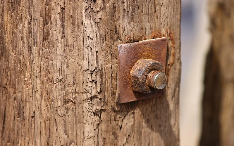 Rusted bolt and washer corroding into a wood post, showing fastener corrosion damage
