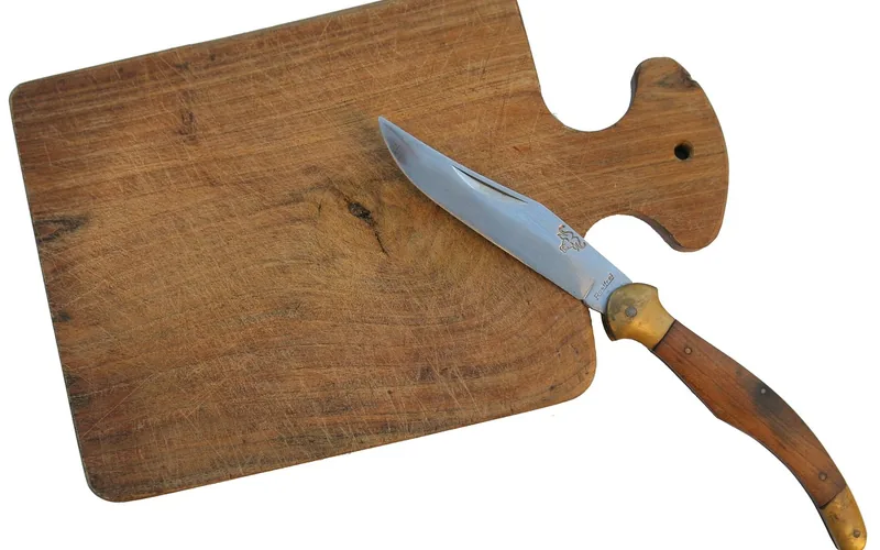 Scarred wooden cutting board with knife a well-used wooden cutting board covered in knife scratches next to a paring knife