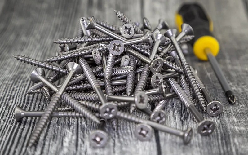 Pile of stainless steel deck screws next to a screwdriver on a workbench