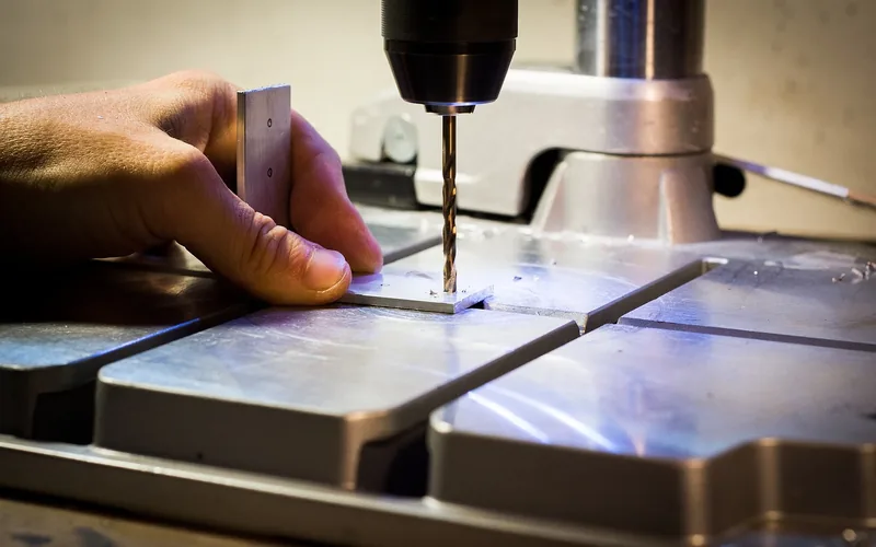 hand drilling a hole through aluminum sheet metal secured on a drill press table