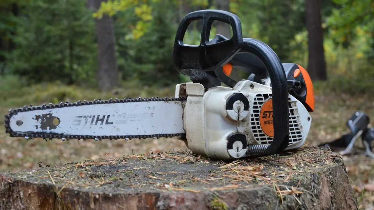 Gas chainsaw with a 2-stroke engine resting on a tree stump in a forest