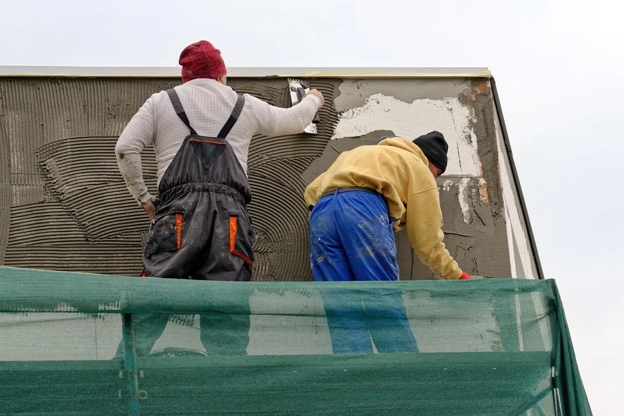 Two workers troweling a cement-based skim coat onto a wall