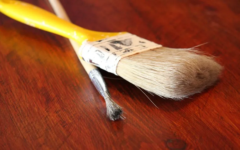 Wide flat brush and narrow brush resting on a stained wooden tabletop Wide flat brush and narrow brush resting on a stained wooden tabletop