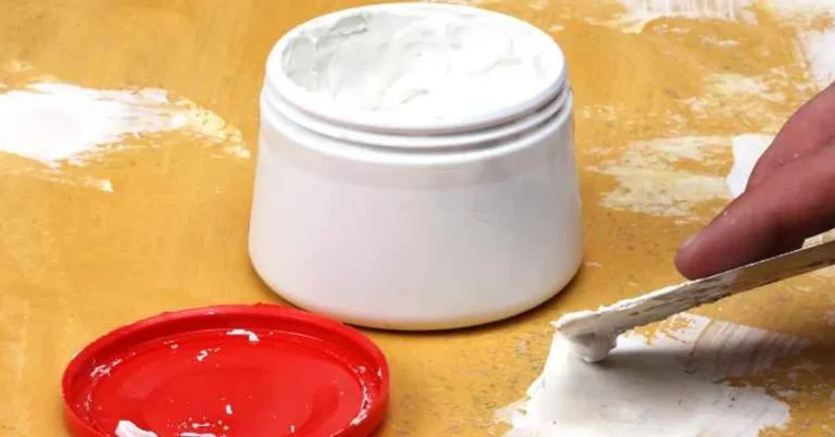 White wood putty in an open tub being applied with a putty knife