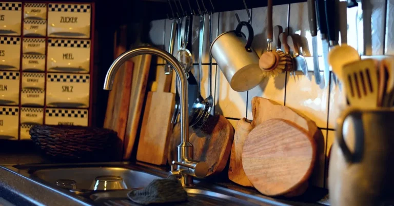 wooden cutting boards resting by a kitchen sink faucet next to a dish brush