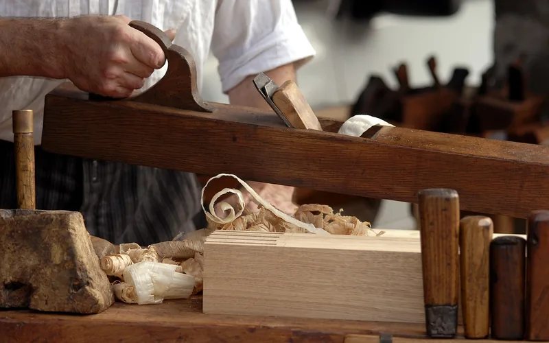 Traditional wooden hand plane cutting a shaving curl off a board edge