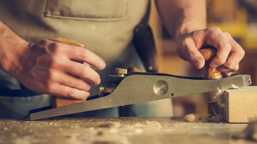 Woodworker planing stock in a home workshop, generating fine dust and shavings