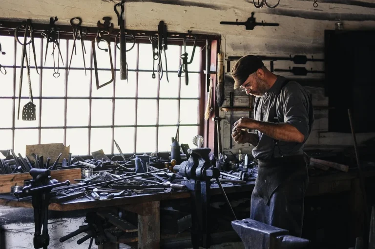 Craftsman in a long work apron standing at his workbench in a tool-filled shop