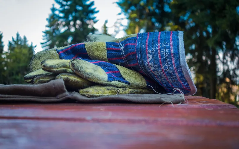 worn leather work gloves resting on a wood surface, used for protection when handling cedar