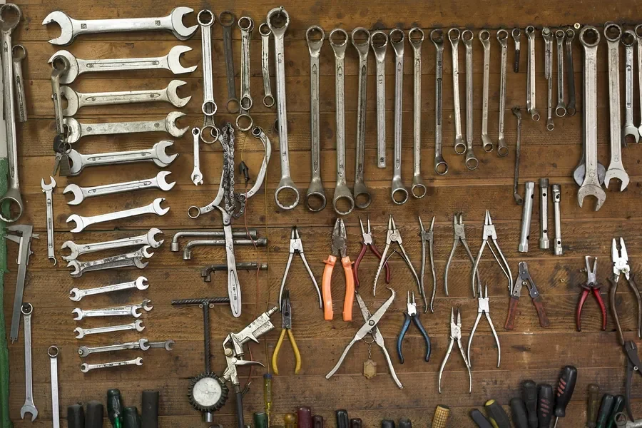 Wrenches, pliers and screwdrivers laid out in rows on a wood panel